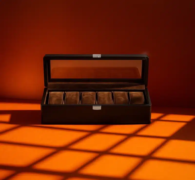 Coffret à montres Abraham de la Maison Garnot en bois foncé avec six compartiments en velours brun, présenté ouvert sur fond orange lumineux